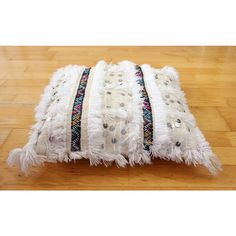 a white pillow with fringes and beads on it sitting on top of a wooden floor