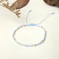 a blue bracelet with gold beads sits on a white surface next to a dried plant