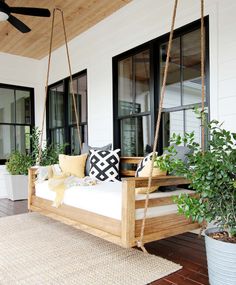 a porch swing with pillows and plants on it