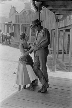 an old black and white photo of a man standing next to a woman on a porch