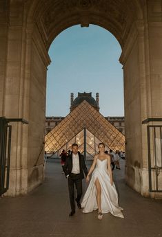 a bride and groom walking under an arch in front of the pyramid