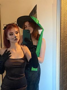 two women dressed up as witches taking a selfie in the mirror with their cell phone