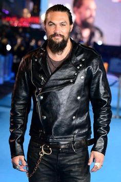 a man with a beard and leather jacket standing in front of a blue carpeted area