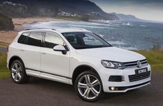 a white volkswagen cayen is parked on the side of the road by the ocean