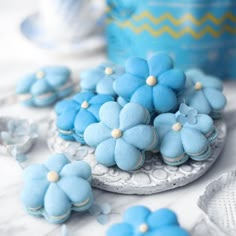 some blue flowers are sitting on a white plate and next to other cookies that look like they have been made from icing