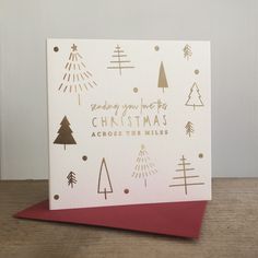 a white christmas card with gold foil trees on it and the words, sending your merry christmas across three miles