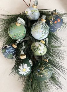 a bunch of christmas ornaments hanging from a pine tree with white and green flowers on them