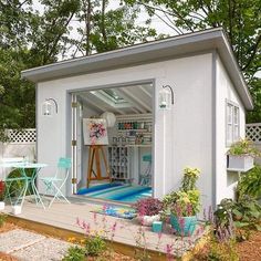 a small white shed sitting in the middle of a yard with lots of plants and flowers