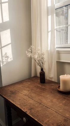 a wooden table topped with a candle and vase filled with flowers next to a window