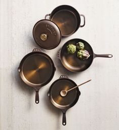 four cast iron skillets with spoons and broccoli in them on a white table