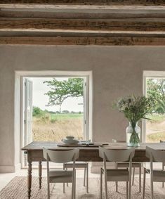 a dining room table with chairs and a vase on the table in front of two windows