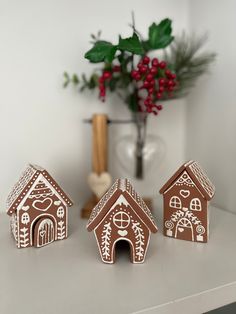 three small gingerbread houses sitting on a table next to a vase with red flowers