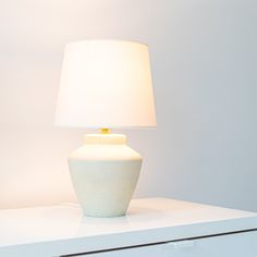 a white lamp sitting on top of a table next to a dresser and drawers in a room