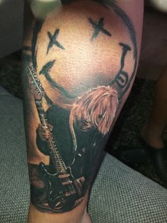 a man's leg with a clock and guitar tattoo on it, while he is sitting down