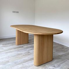 an oval wooden table in a room with white walls and wood flooring on the ground