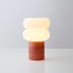 an orange and white table lamp sitting on top of a white counter next to a gray wall