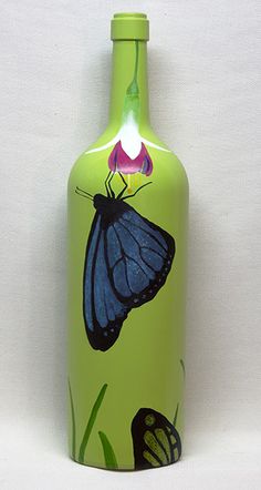 a green glass bottle with a butterfly painted on the front and side, sitting against a white background