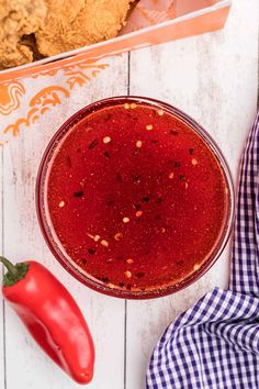 a red sauce in a glass bowl next to a spoon and some chili peppers on a white wooden table