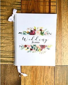 a wedding planner with flowers on it sitting on top of a wooden table next to a pen