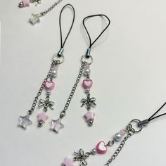 three necklaces with charms and hearts hanging from them on a white surface, one is pink