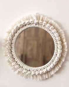 a white round mirror with tassels hanging on the wall