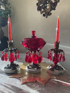 three red candles sitting on top of a table next to a candle holder and some leaves