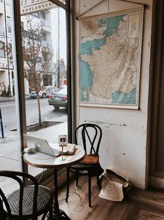 two chairs and a table in front of a window with a map on the wall