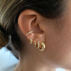 a close up of a woman's ear with three gold earrings on top of it