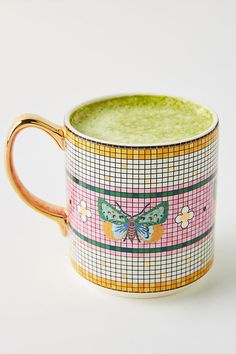 a cup with a butterfly painted on the side and gold trim around the edge, sitting on a white surface