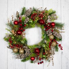 a christmas wreath hanging on the side of a white wooden wall with red and green ornaments