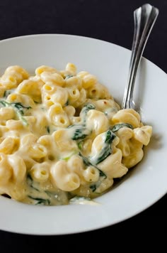 a white plate topped with pasta and spinach covered in sauce next to a fork