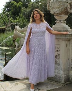 a woman standing next to a fountain wearing a purple dress and shawl over her shoulders