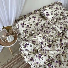 an unmade bed with purple flowers on it