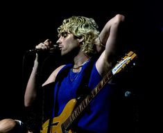 a man with blonde hair and blue shirt holding a yellow guitar in his right hand