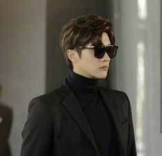 a man in a black suit and sunglasses looking off to the side with one hand on his hip