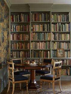 a table and chairs in front of a bookcase filled with lots of books on shelves