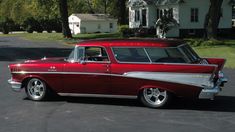 an old red and white car is parked in the parking lot next to a house