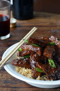 meat and rice on a white plate with chopsticks next to it, sitting on a wooden table