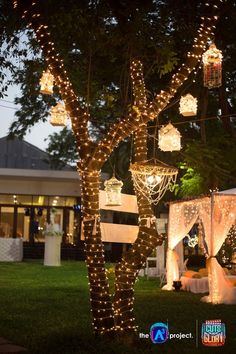 an outdoor wedding venue decorated with fairy lights and hanging lantern lanterns on the tree trunk