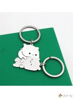 a metal keychain with a white teddy bear on it's side, sitting on top of a green folder