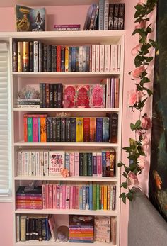 a bookshelf filled with lots of books next to a window covered in pink flowers