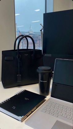 an open laptop computer sitting on top of a white desk next to a black bag