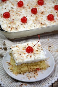 a piece of cake with white frosting and cherries is on a plate next to a casserole dish