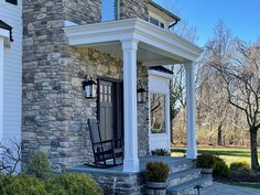 a rocking chair sitting on the front porch of a stone house with columns and pillars