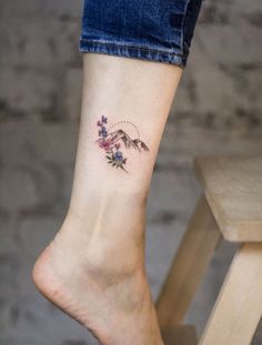 a woman's foot with a small tattoo on her left ankle and mountains in the background