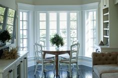 a dining room table and chairs in front of large windows