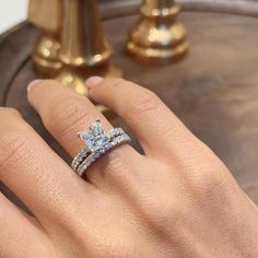 a woman's hand with a diamond ring on top of her finger, next to a gold pedestal