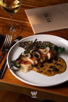 a white plate topped with food on top of a wooden table next to a glass of wine