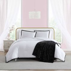 a bed with white and black comforters in a pink room next to a window