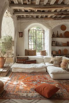 a living room filled with lots of furniture and pillows on top of a rug in front of a window